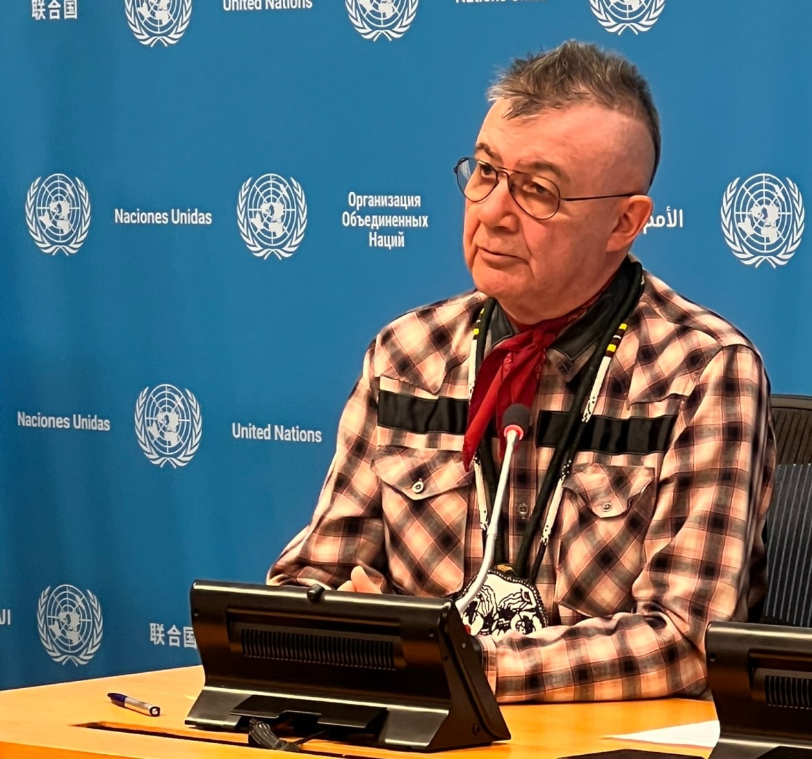 A man sitting at a desk in front of a United Nations backdrop.
