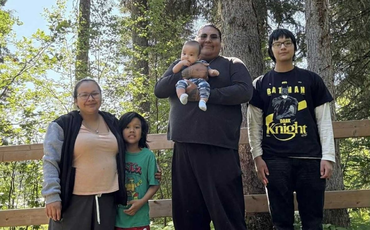 A man poses with a three children an woman in front of a forest.
