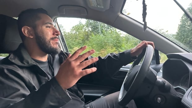  A man in the drivers seat of an SUV with the left hand on the steering wheel and gesturing with the right hand.