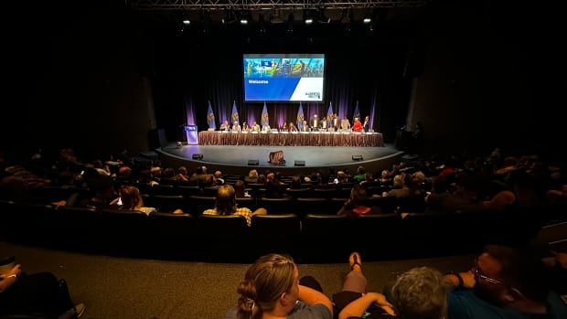 A dark, half-full, theatre-like room of audience members.