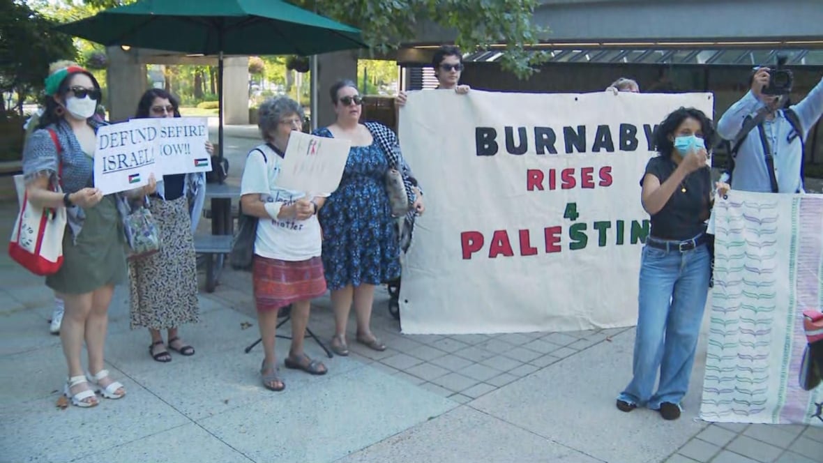 A small group of people hold up signs reading 'Burnaby Rises 4 Palestine'.