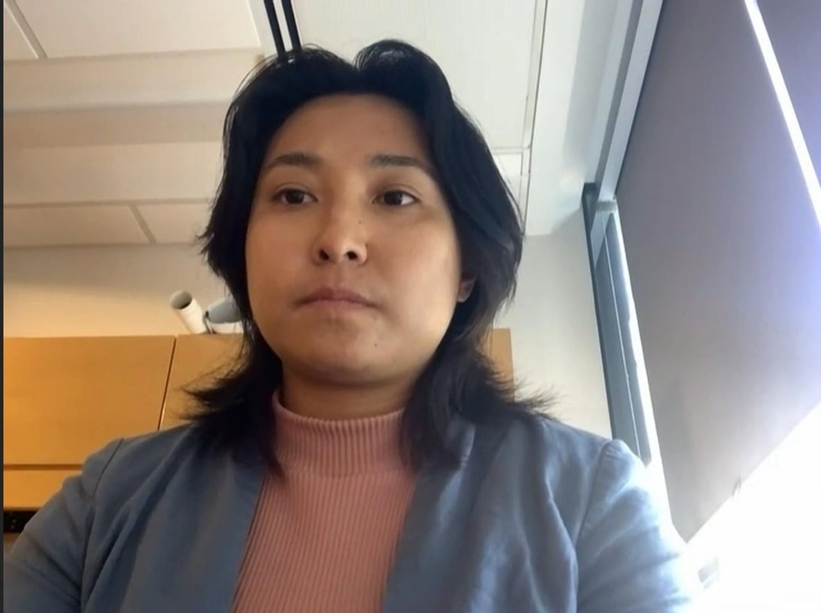 A woman wearing a turtleneck sweater speaks.