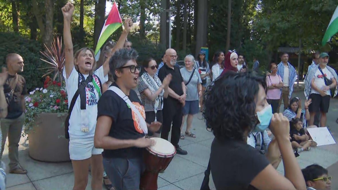 A few dozen people are seen chanting and playing drums.
