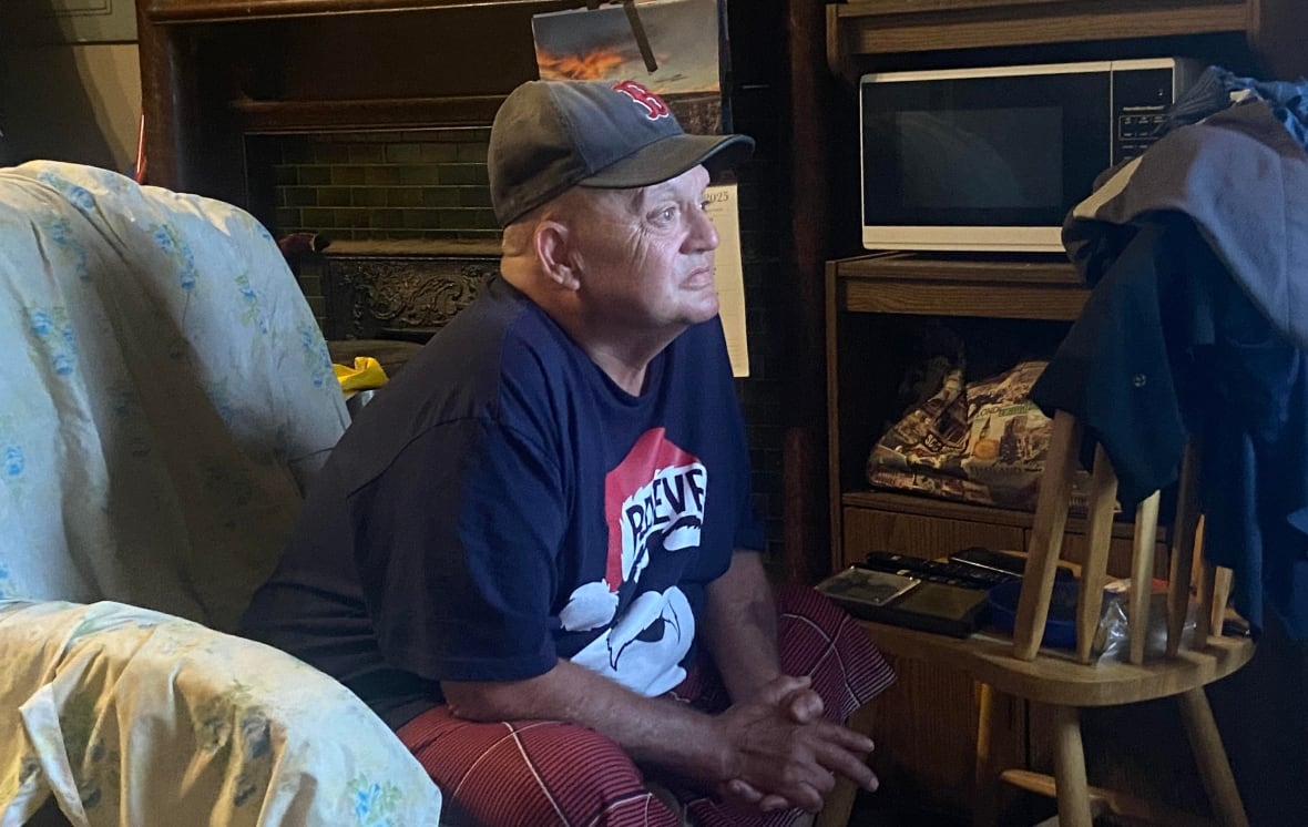 older man facing to the right, wearing baseball cap and sitting in an armchair