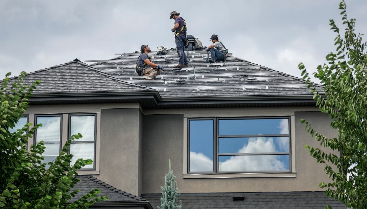 Three workers who install metal rails on a roof of a house.