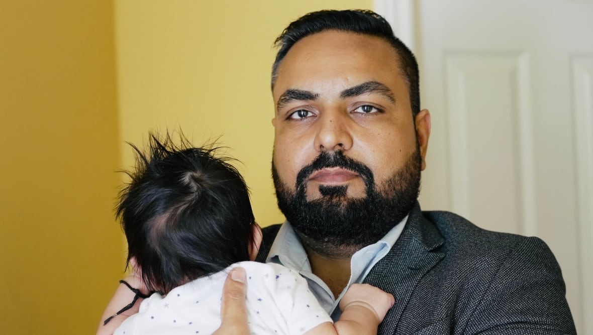 Gurinder Sidhu looks at the camera while holding his baby.