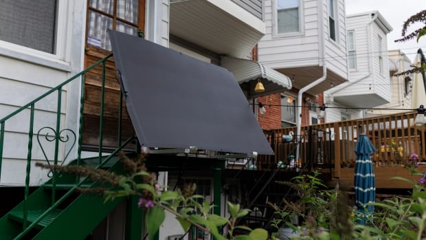 A solar panel from Bright Saver hangs at Craig Keenan's home Friday, Aug. 1, 2025, in Baltimore. A black solar panel hangs off a the rail of a stairway landing outside the entryway to a house.