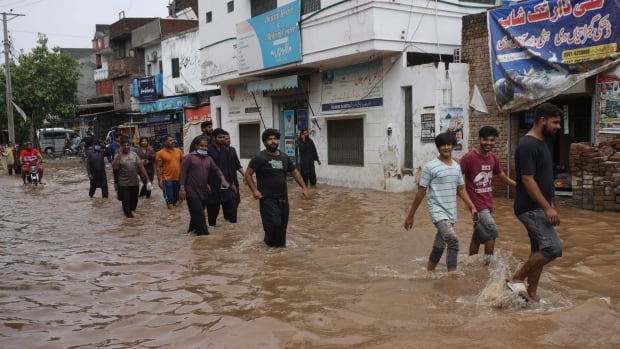 A row of people wade through water that goes up mid-calf on a flooded street. 
