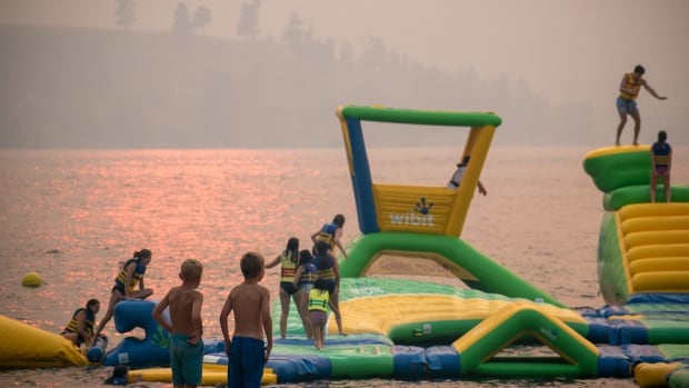 Children play on the water amid an orange, smoky sky.