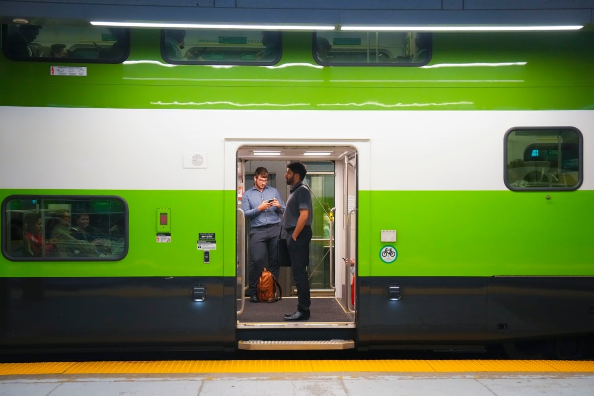 Two men stand in the doorway of a green train stopped at a platform