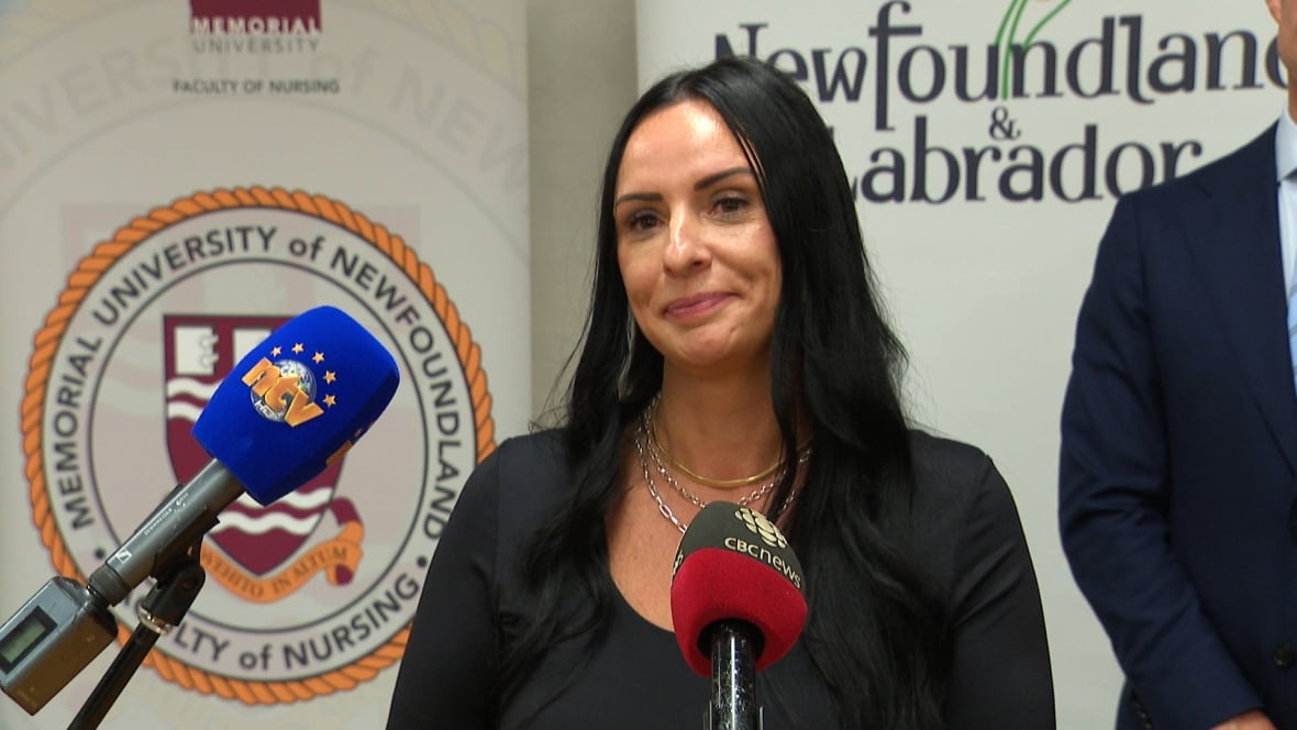 A smiling woman stands in front of microphones at a press conference.