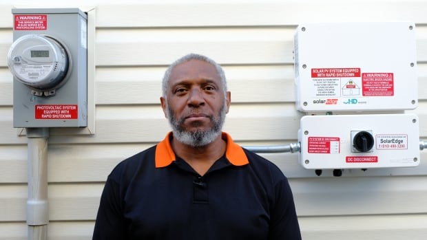 Jay Hector stands beside part of the solar panel system installed at his Calgary home on Aug. 26, 2025. Hector paid more than triple the average industry rate for the system and is warning others to do their research before signing a contract with door-to-door salespeople. A man stands in front of an electricity meter and a solar power system mounted on the side of his home.