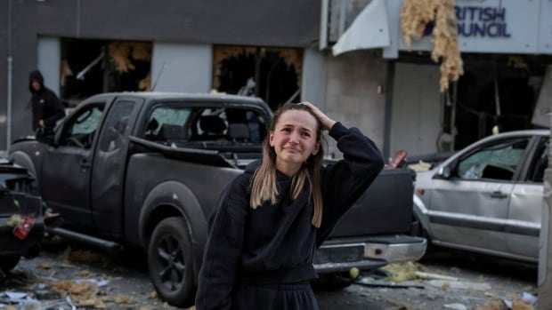 A woman in a black sweatsuit cries as she holds a phone in one hand and her head in the other.