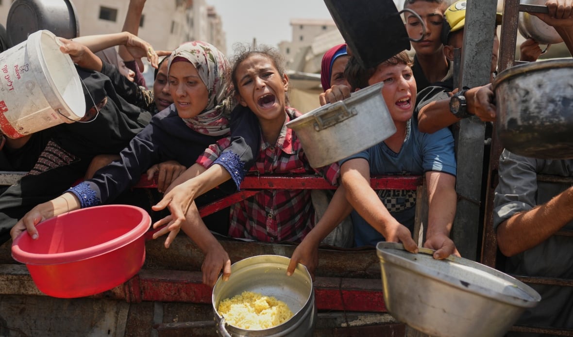 A group of people, including children, carry large vessels at a barrier towards the camera, and look like.