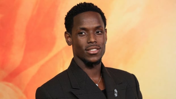 A man in a dark suit smiles and looks slightly past the camera to his left at a red carpet premiere event