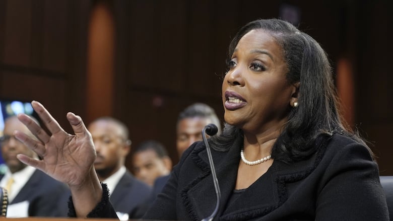 A woman talks to a microphone with one hand. A crowd of other people is her view.