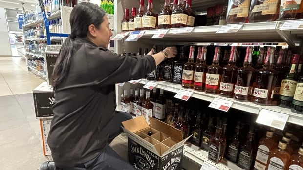 A liquor store employee is shown removing a bottle of whiskey from a store shelf.