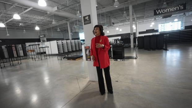 A woman dressed in red coat and black pants at a huge empty warehouse building.