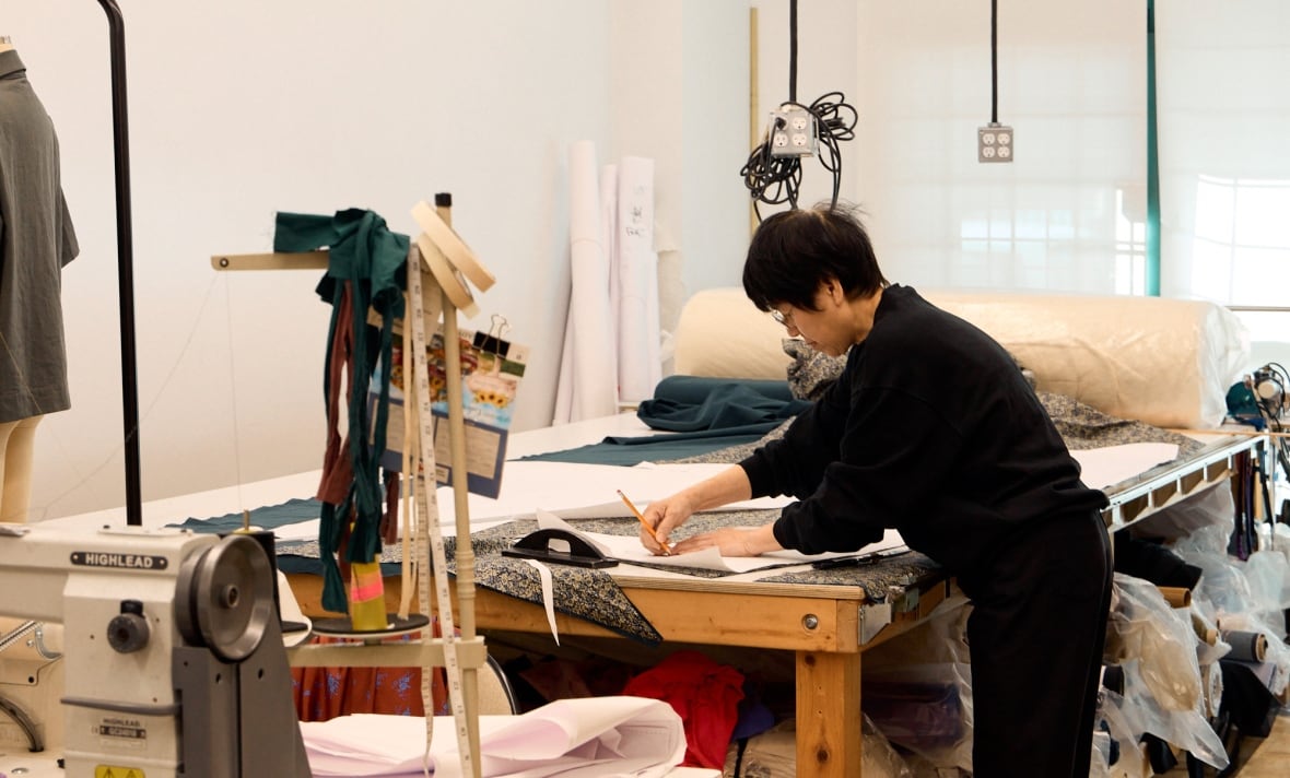 The woman uses a pencil and paper to track the pattern over the dress on the table.