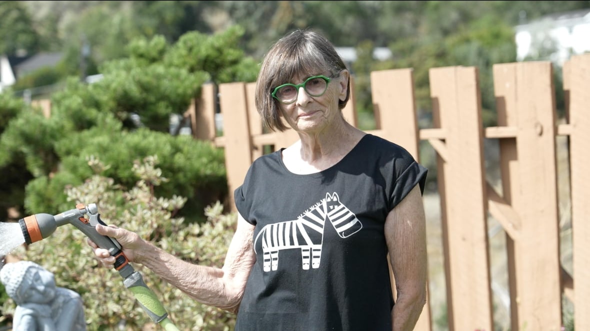 A woman with hair to her chin and green glasses holds a garden hose.