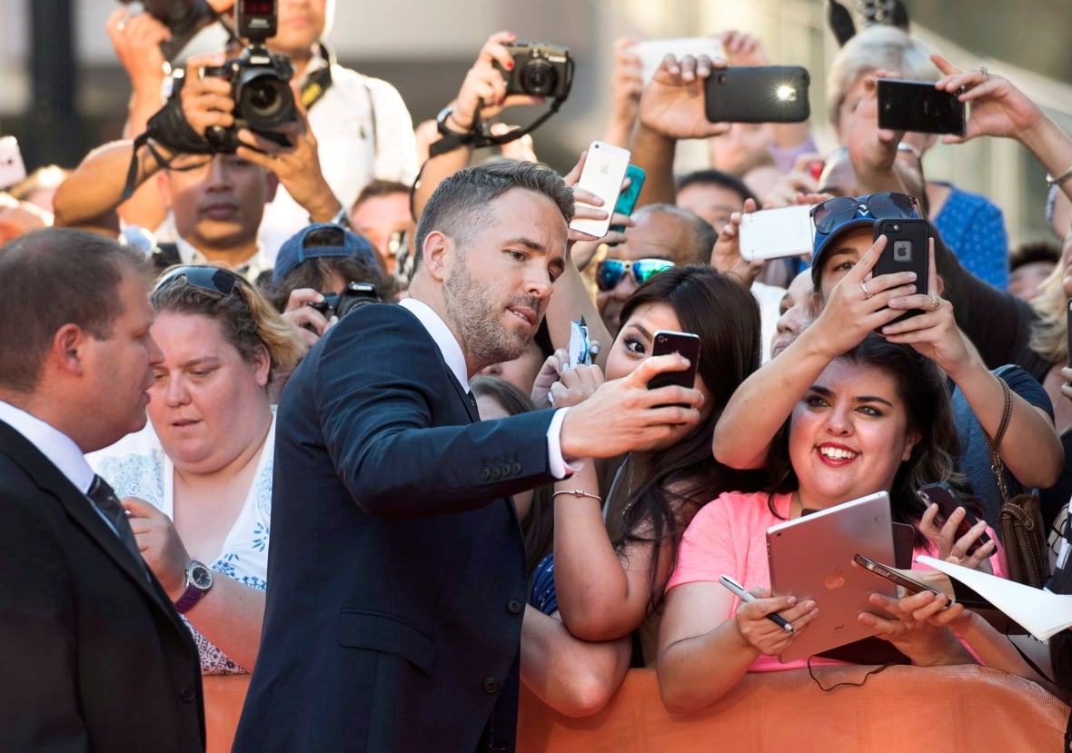 Aktor Ryan Reynolds w garniturze robi sobie selfie z fanami na czerwonym dywanie TIFF w 2015 roku