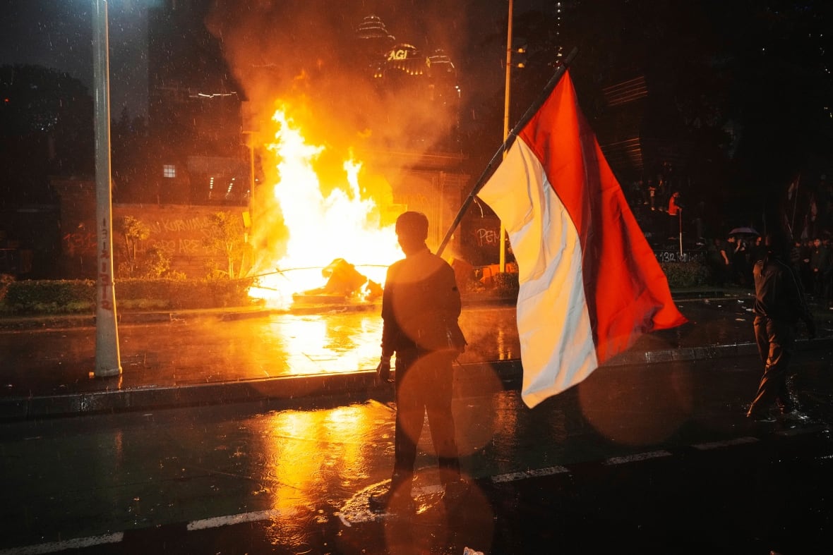 A man holds the flag standing in the street in front of the fire