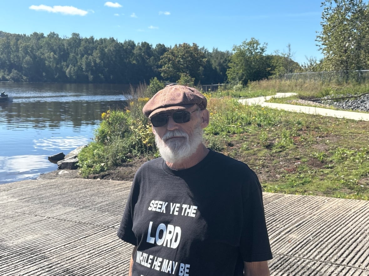 A man with a black shirt and a brown cap and sunglasses, which has a white beard.