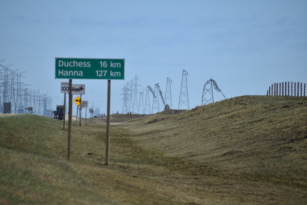 A road sign in the foreground shows distance to Duchess and to Hanna. In the distance, several power transmission towers are bent over in half. 
