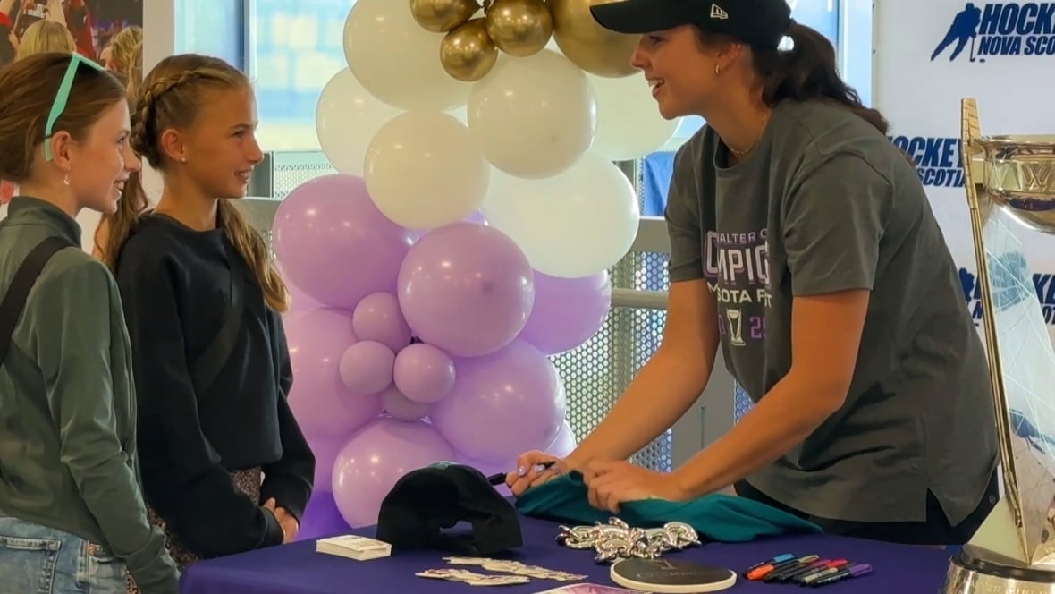 Mae Batherson talks to two girls while signing a hockey jersey for them. 