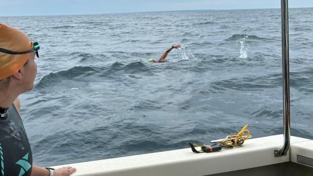A swimmer working to complete the ninth leg of the Edmund Fitzgerald Memorial Swim Person swims in water while onlooker watches from a boat.
