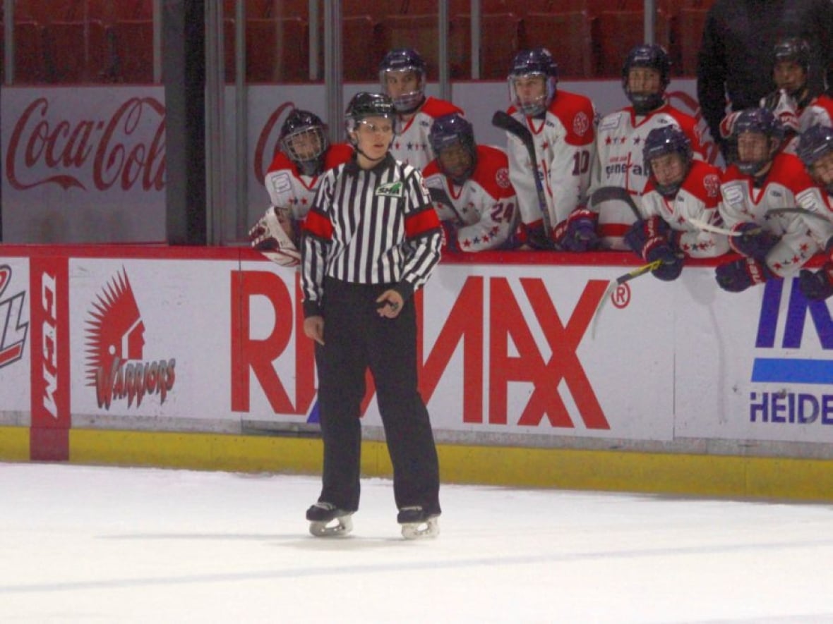 A referee on the ice in front of a player's bench.