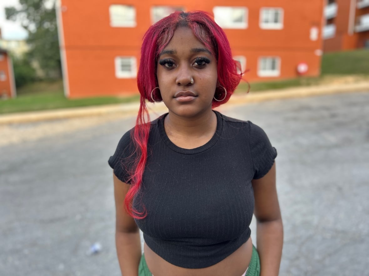 Laniyah King is 17 years old. It has a colored Fosha hair associated again in a low ponytail. The explosions are cut in the middle. She wears the top of a black crop and green pants. It stands in front of a red brick building.