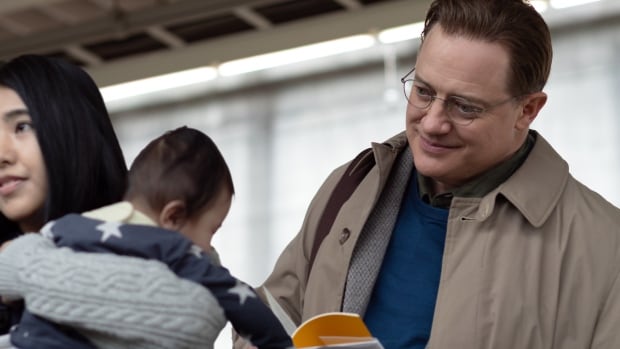 A smiling man holds a book while looking at a baby.