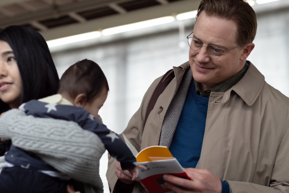 A smiling man holds a book while looking at a baby.