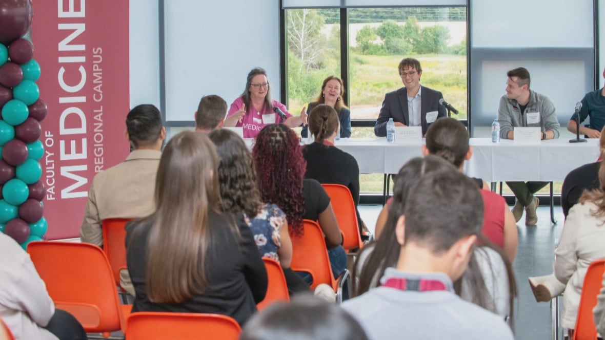 Several students are seen from behind while listening to a speaker table.