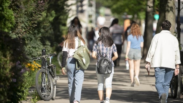 Quebec universities are worried by a drop in international student applications brought on by tighter immigration rules. People walking on a sidewalk lined with greenery.