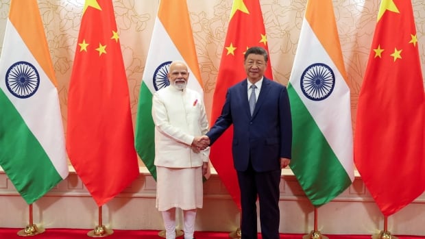 The Indian prime minister on the left shakes hands with the Chinese president on a red carpet in front of each of the country's flags.