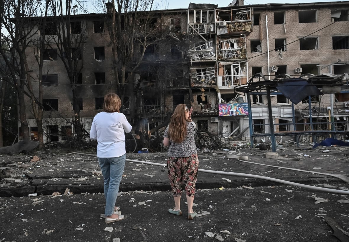 Two women look at a residential building damaged by the bombing. 