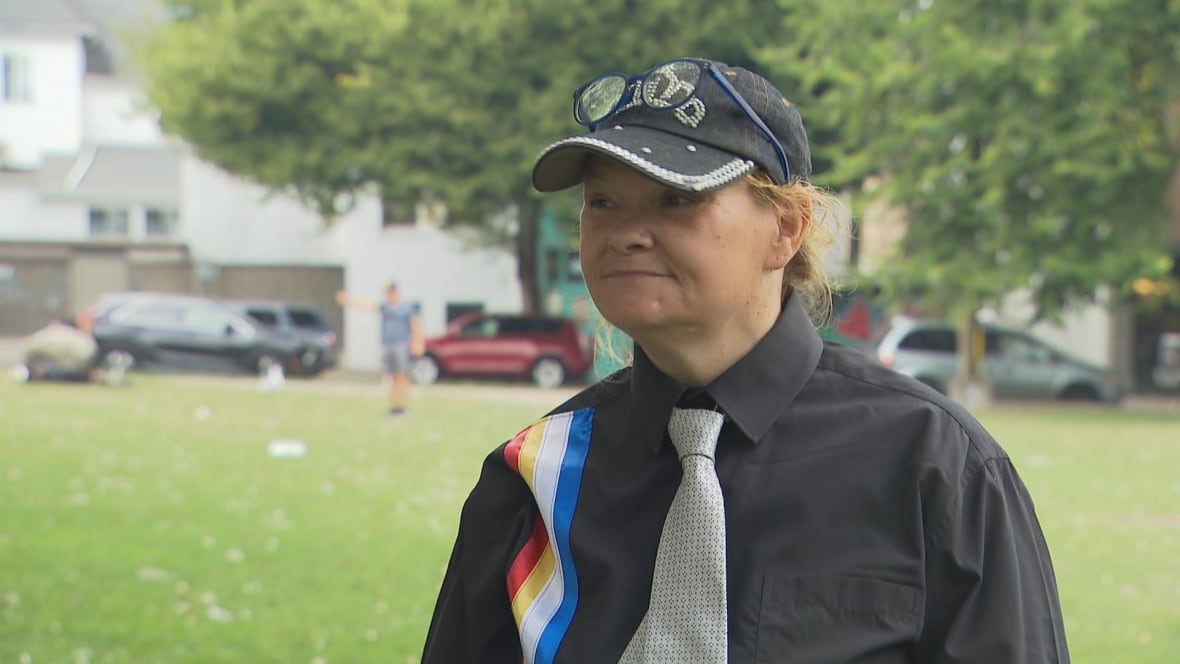 A woman wearing a black shirt and white tie smiles in a park.