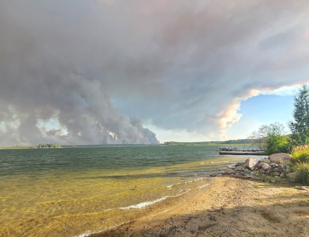 Wildfire smoke can be seen across a lake, billowing past some blue sky. 