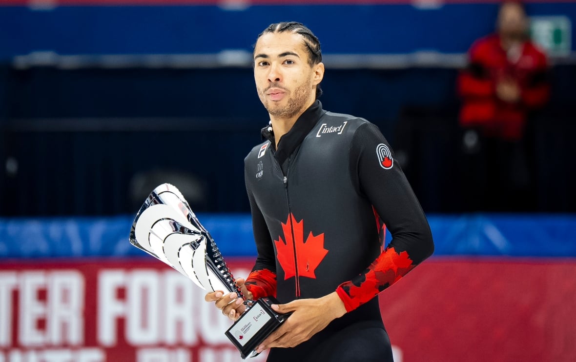 A men's speedskater holds a trophy.