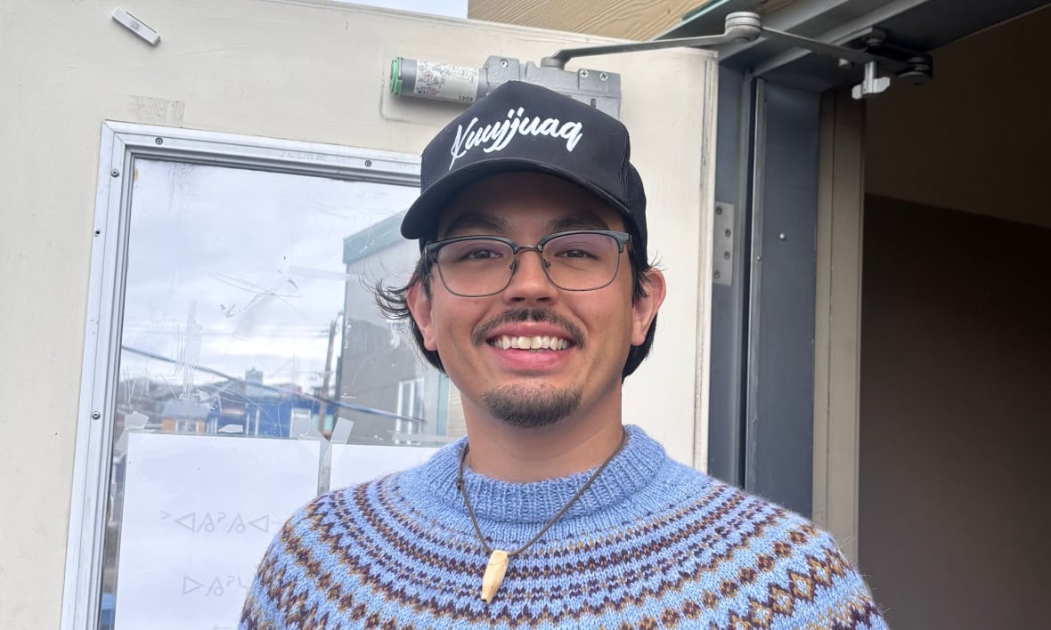 The man with blue sweater and the baseball is smiling in front of the community center.
