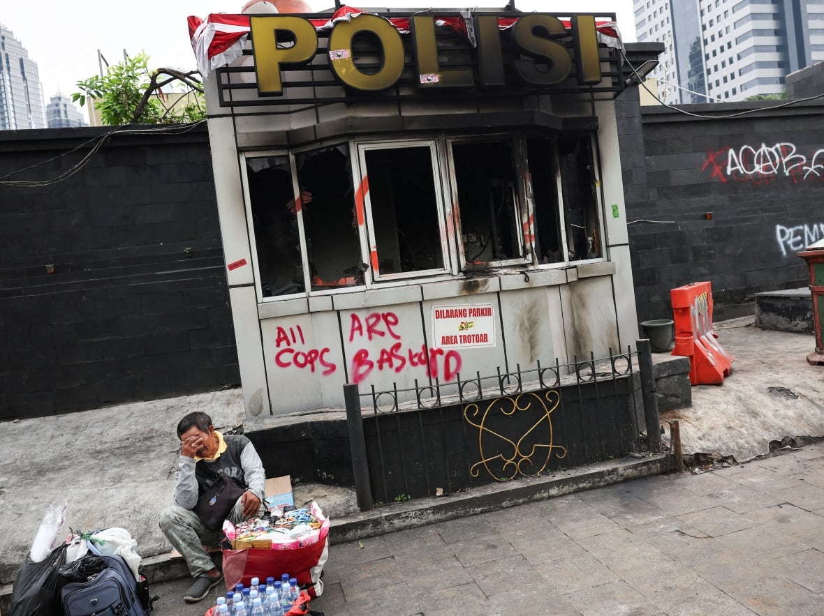 A person sits in front of a burning police station.