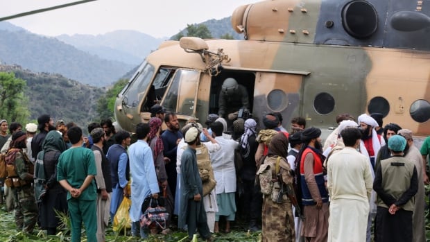 Dozens of people, many men in robes, stand around a helicopter in a grassy area.