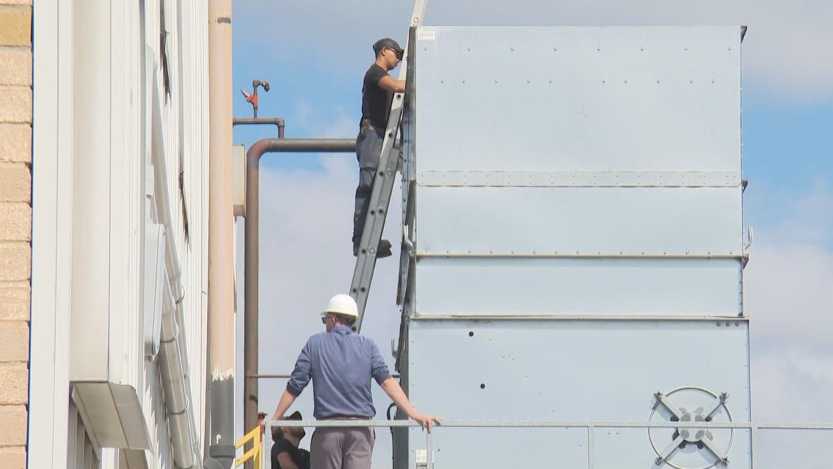 One person stands on a ladder that looks at a cooling tower while another is underneath.