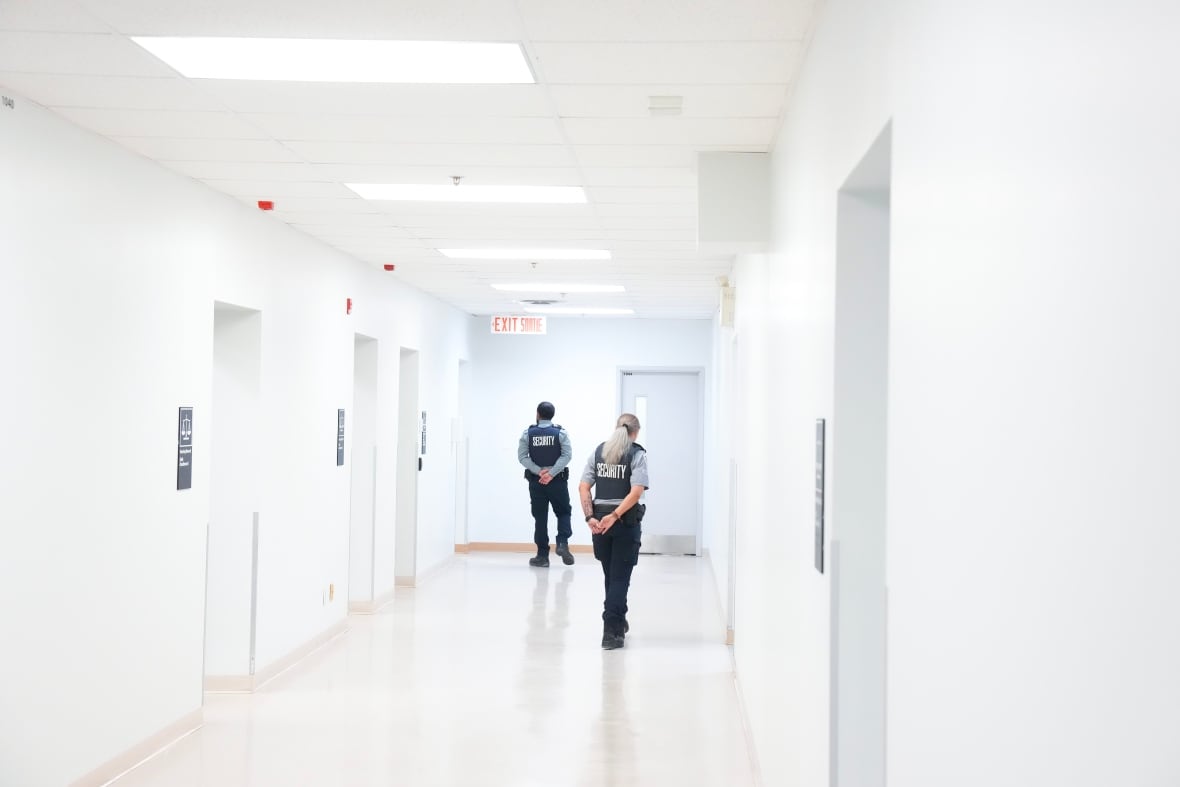 Dos guardias de seguridad caminan por un pasillo blanco en un centro de retención de inmigración en Toronto.