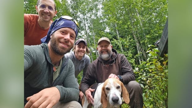 Four people and a dog take a selfie in a wooded area.