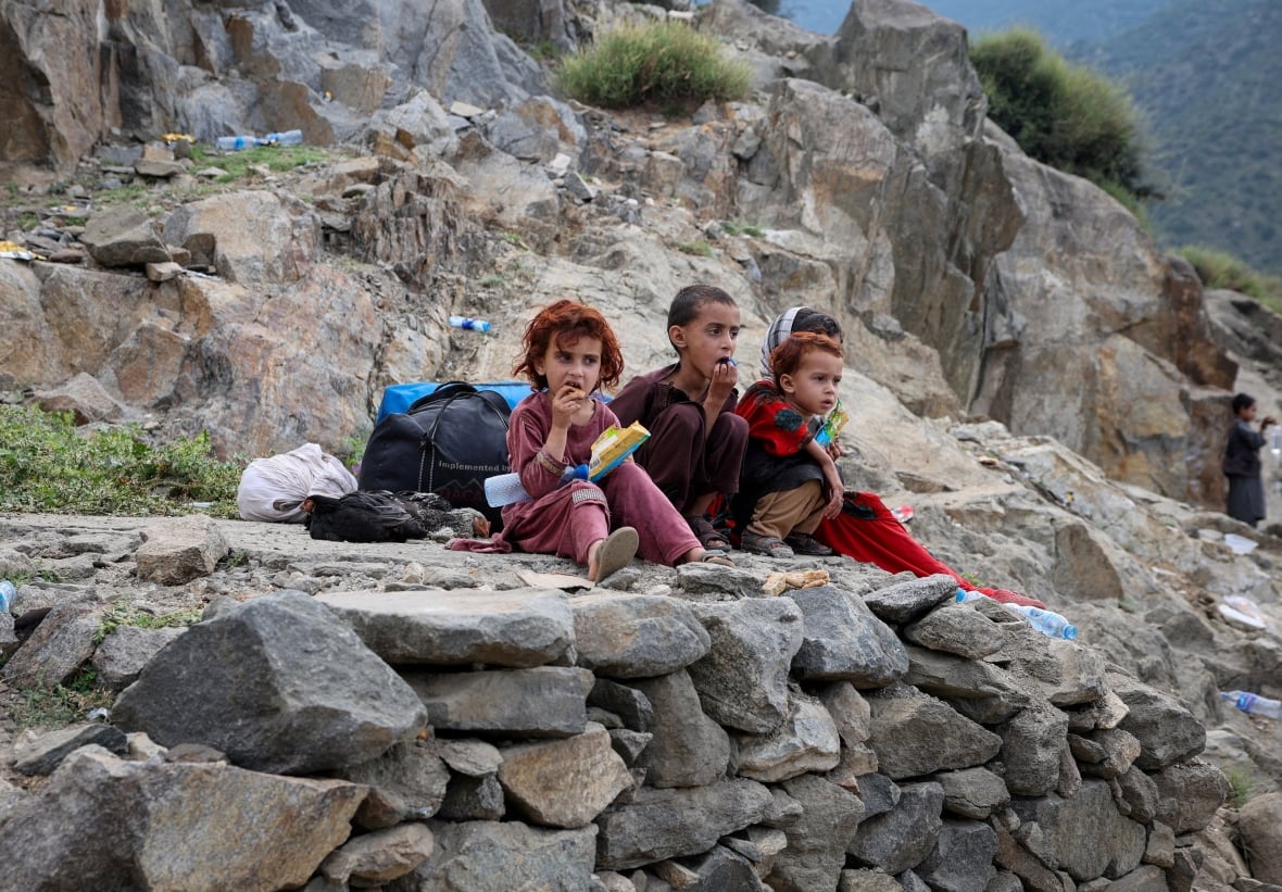 Four young children sit alone on a rock with bags around them