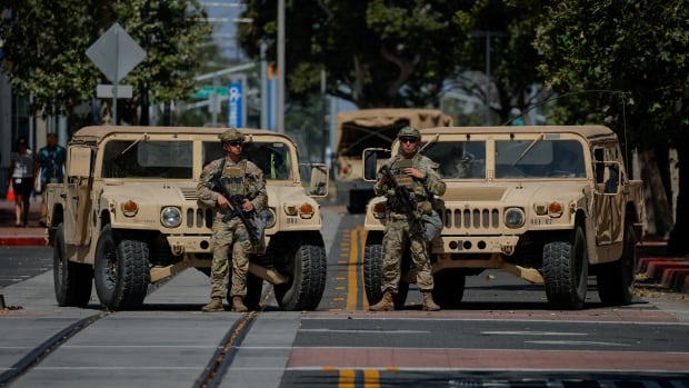 Individuals dressed in camo stand in front of tan coloured Jeeps with large guns
