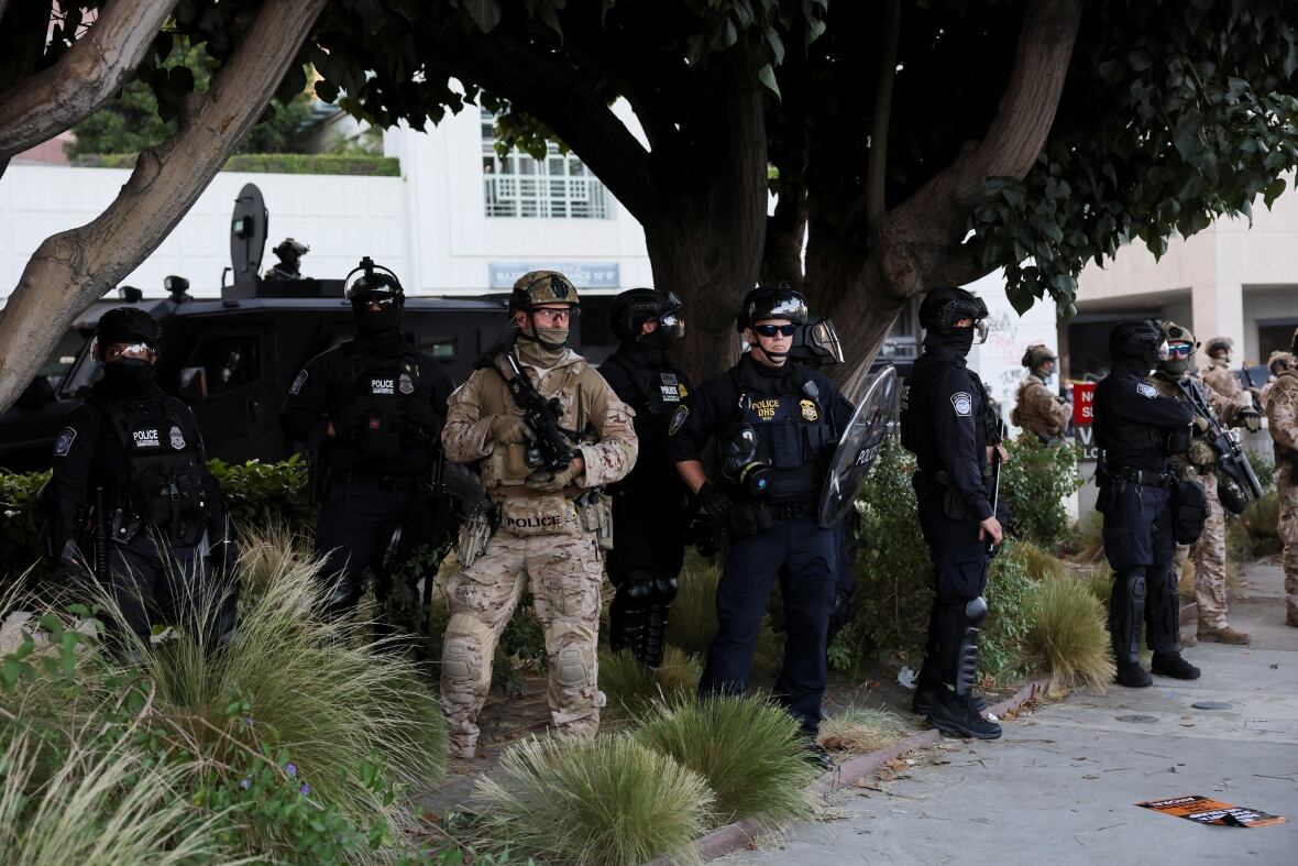Man Incamunu stands with a large rifle along police officers wearing blue outfit